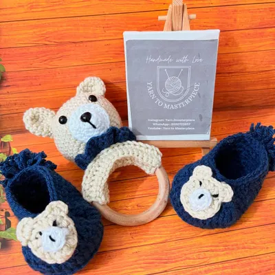 This adorable baby boy set includes a pair of navy blue booties with bear faces and a matching bear rattle. It's made from soft, safe yarn, perfect for a newborn gift.