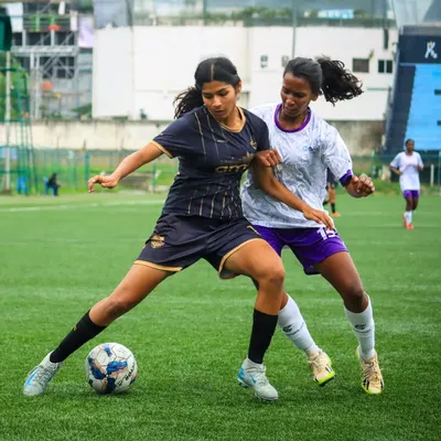 A girls' school football match in full swing, with a player skillfully shielding the ball from a defender during a competitive game.