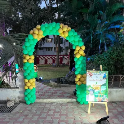 A beautiful outdoor entrance for a jungle-themed party, with a green and yellow balloon arch and a personalized welcome sign set against a park backdrop.
