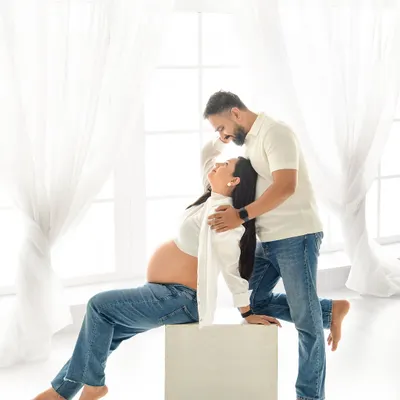 A playful and intimate moment between the expecting couple. Dressed in casual jeans and white shirts, they share a laugh in our bright, sunlit studio, creating a relaxed and authentic portrait.