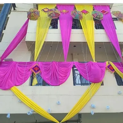 An example of our house exterior decoration for a wedding. We use bright pink and yellow drapes, along with decorative umbrellas and hangings, to adorn the building's facade.