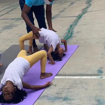 An instructor provides gentle guidance during an outdoor yoga session, helping a young student perfect her backbend on a yoga mat.