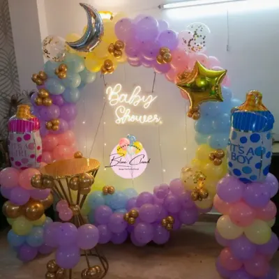 A gorgeous pastel-themed baby shower decoration with a full balloon ring. This setup includes a 'Baby Shower' neon sign and foil balloons shaped like baby bottles.