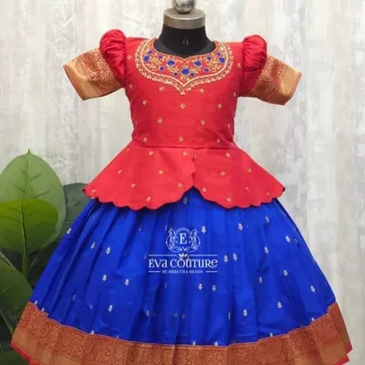 A vibrant pattu pavadai with a modern peplum top. The red blouse has intricate maggam work, and it pairs beautifully with the royal blue skirt that has a traditional gold zari border.