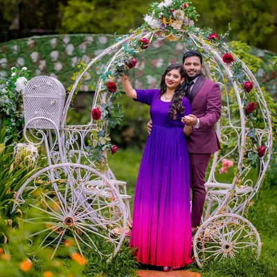 A classic fairy tale moment. This couple shares a dance in front of a whimsical white carriage, decorated with red roses. The bride-to-be's ombre gown adds a beautiful splash of color to the scene.