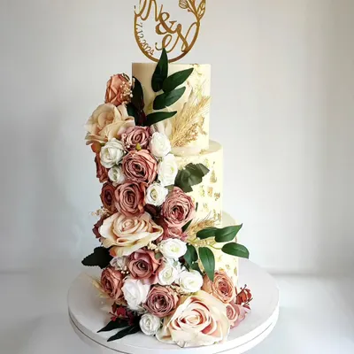 A breathtaking three-tier wedding cake featuring a cascade of dusty rose and cream flowers. This design is the epitome of romance and elegance, perfect for a grand celebration.