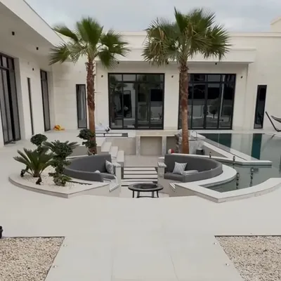 A complete view of a luxury villa's outdoor space, featuring a sunken seating area, a pristine pool, and carefully placed palm and bonsai trees to create a modern oasis.