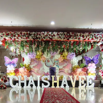 A grand butterfly-themed stage decoration for a large celebration. I used a full floral and balloon arrangement, a red carpet entrance, and large illuminated letters for the birthday girl's name.