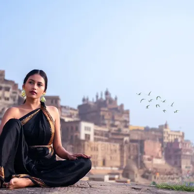 A moment of peace against the timeless backdrop of the Banaras ghats. The elegance of the black saree contrasts with the ancient city, creating a portrait of serene contemplation.