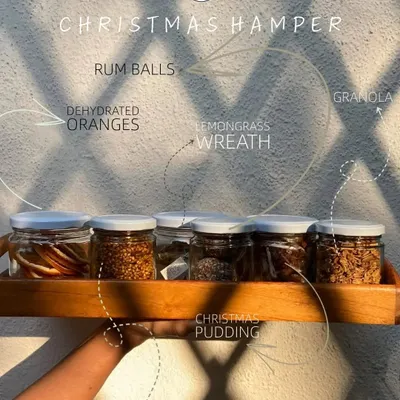 A look inside our Christmas hamper. It features a variety of our handmade goodies like rum balls, granola, Christmas pudding, and even a lemongrass wreath, all beautifully arranged.