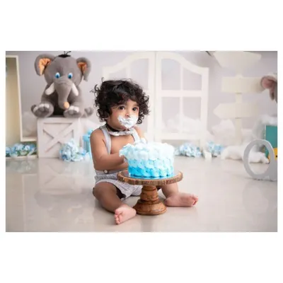 A classic cake smash moment! This little boy is curiously poking his first birthday cake in a beautiful, simple studio setup with blue and white decorations.