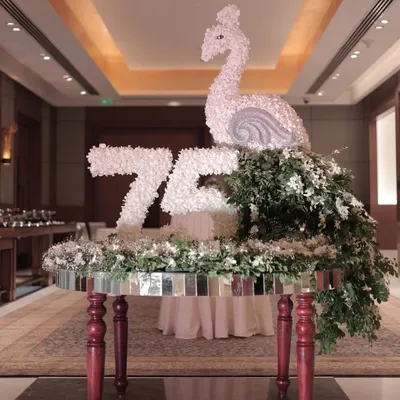 A full view of the custom floral sculpture we created for a 75th birthday. The piece, featuring a swan and the number "75" made entirely of white flowers, sits atop a mirrored table, serving as a magnificent focal point.