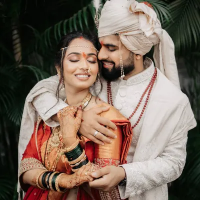 An intimate portrait of a Maharashtrian couple, the groom embracing his bride, who is adorned in a traditional red saree and jewelry.