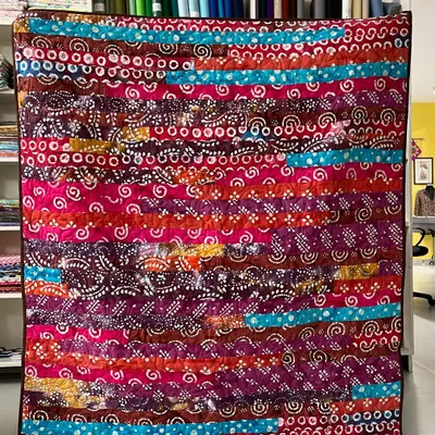 A vibrant "jelly roll" quilt made with strips of colorful, patterned fabric, creating a lively and energetic design.