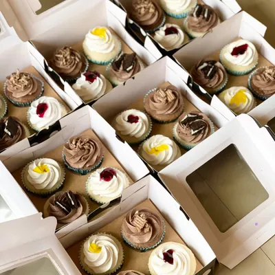Boxes of assorted cupcakes ready for a large corporate order. This is a great way to treat the whole office, with a mix of flavors like chocolate, blueberry, and lemon.