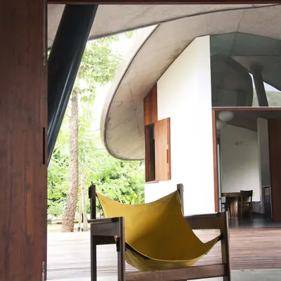 In 'The Leaf House', the living space opens completely to the wooden deck and surrounding trees. The curved concrete roof provides shelter while feeling as light and organic as a canopy of leaves.