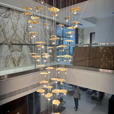 This magnificent cascading chandelier is the centerpiece of a double-height foyer. Each leaf-like element is crafted from gold-toned metal, creating a stunning sculptural light fixture that is both art and illumination.