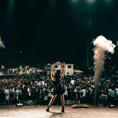 The energy of a live show. Dhvani Bhanushali commands the stage in a custom black fringed top from Seraphine Design Studio, surrounded by smoke and spotlights.