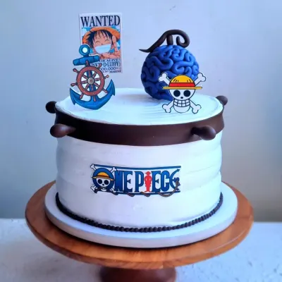 A whipping cream cake with a "One Piece" anime theme. The cake is decorated with printed toppers of the logo, a wanted poster, and a sculpted Devil Fruit.