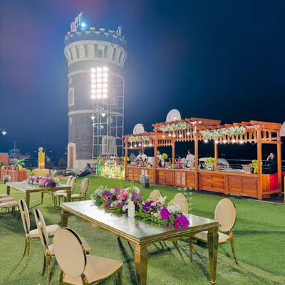A stunning outdoor event space with our rustic wooden food counters set against the backdrop of a historic tower. The elegant guest seating in the foreground shows how we integrate our catering setup into the overall event design.