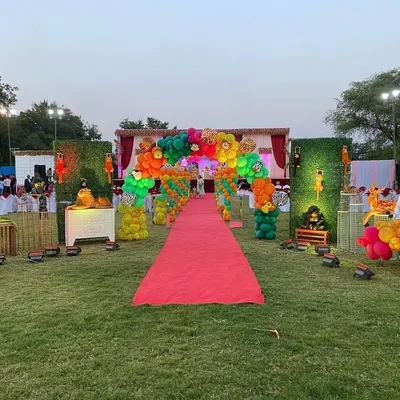 A grand entrance for a jungle party at a farmhouse, featuring a red carpet walkway lined with green hedge walls, animal props, and vibrant balloon arches.
