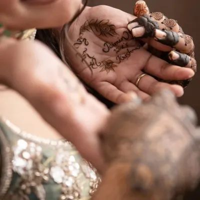 The process begins. Our artist carefully applies the couple's names, 'Jaimin & Krishna', on the bride's palm. This is the start of a beautiful, personalized design.