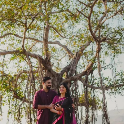 A stunning wide shot of the couple standing beneath the sprawling branches of a majestic banyan tree. This image uses nature as a grand, symbolic backdrop for their pregnancy journey, highlighting their connection to each other and the world around them.