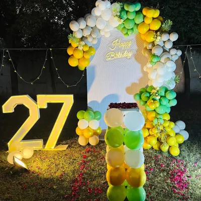 A beautiful outdoor birthday setup for a 27th birthday. This decoration features a balloon arch, a "Happy Birthday" neon sign, and large light-up numbers with the name "Amar".