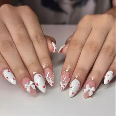The cutest coquette-style nails. This set features white tips, tiny red hearts, and adorable 3D white bows.