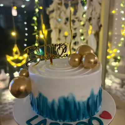 A stylish birthday cake with a teal brushstroke effect and gold sphere decorations.