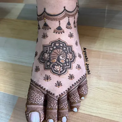 A minimal yet elegant bridal foot design. This mehendi features a central peacock motif with delicate hanging 'jhumkis' and simple patterns on the toes.
