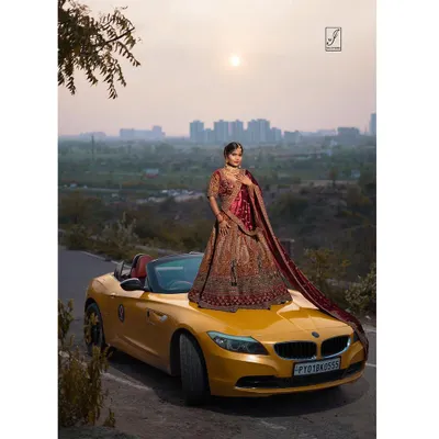 A full-length shot showcasing an intricately embroidered bridal lehenga. Posing the model on a luxury car adds a modern, aspirational twist to traditional bridal photography, creating a truly unique campaign image.