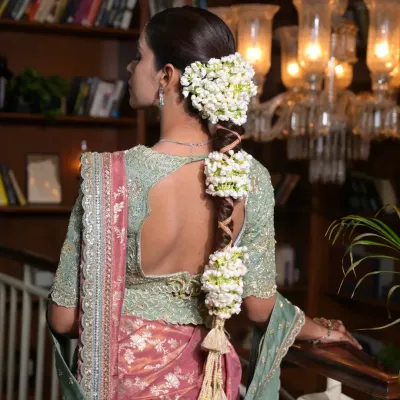 A detailed profile of a traditional South Indian bridal hairstyle. The focus is on the thick, woven gajara braid, heavily adorned with fragrant jasmine flowers for an authentic and rich look.