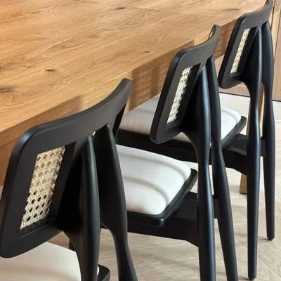A set of my custom dining chairs with black frames, white cushions, and a cane back detail, paired with a solid oak table. This is a great example of my modern dining furniture.