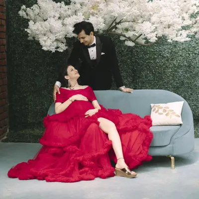 A glamorous maternity look for a studio photoshoot. The mom-to-be looks stunning in a bold red gown, with makeup that highlights her features and gives her a radiant glow.