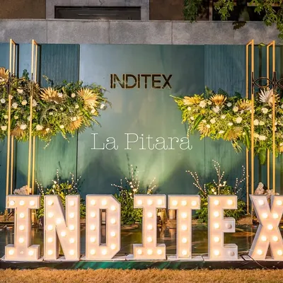 A stunning photo backdrop designed for the Inditex Diwali party, featuring large marquee letters of the company name. The setup is framed by modern gold structures with lush floral arrangements, creating a perfect spot for corporate branding and guest photos.