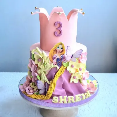 A magical Rapunzel-themed cake for a third birthday. This design features a crown-shaped top tier, a fondant Rapunzel figure, her long braided hair, and beautiful sugar flowers and butterflies.