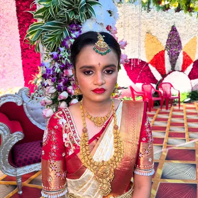 A classic muhurtham look for Priyanka in her beautiful white and red Kanjeevaram saree. The makeup features a bold red lip and defined eyes, perfectly complementing her traditional gold jewellery.