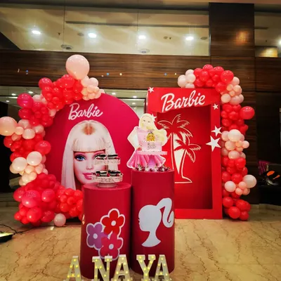 A classic Barbie theme for a fun birthday party. This setup features a round backdrop with the iconic Barbie face, a doll box photo prop, and a red and pink balloon garland.