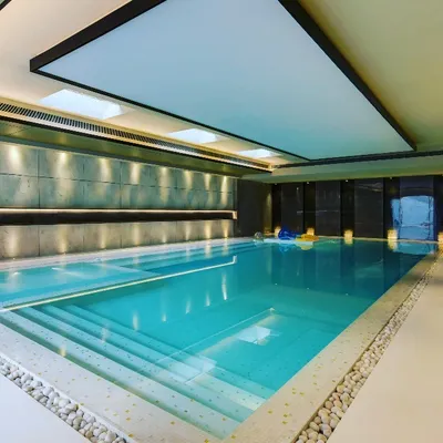 An alternate view of a serene indoor swimming pool, highlighting the stepped entry and the clean, minimalist finish of the surrounding floor. The thoughtful lighting and material choices create a tranquil space dedicated to health and relaxation, accessible in any season.