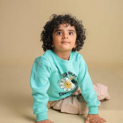 A simple and sweet studio portrait of a toddler with beautiful curly hair, looking up with a curious expression. The neutral background keeps the focus entirely on the child.
