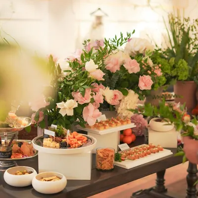 A wide view of our elegant catering setup for the Gauri & Nainika launch event. The table is a landscape of flavors, featuring tiered displays of canapés, cheese platters, and fresh floral arrangements, designed to impress guests.