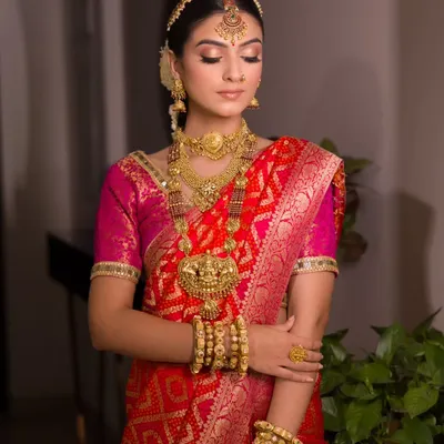 The complete vision of a South Indian bride. Dressed in a traditional red and pink silk saree with magnificent temple jewellery, her makeup is kept classic and golden to enhance her divine look.