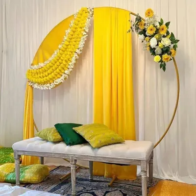 This haldi setup combines traditional elements with a modern design. The circular frame is a fantastic backdrop for photos, and I've used classic yellow drapes and genda phool (marigold) garlands to create that perfect, happy haldi vibe.