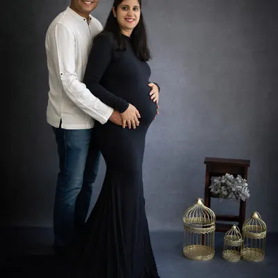 A classic and elegant studio maternity portrait. The simple, dark attire emphasizes the baby bump, creating a timeless image that celebrates the beauty of pregnancy.