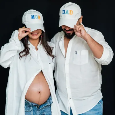 Studio sessions can be fun and modern. Using simple props like 'Mom' and 'Dad' caps, we created a playful and stylish portrait that shows off the baby bump and the couple's personality against a clean, classic black backdrop.