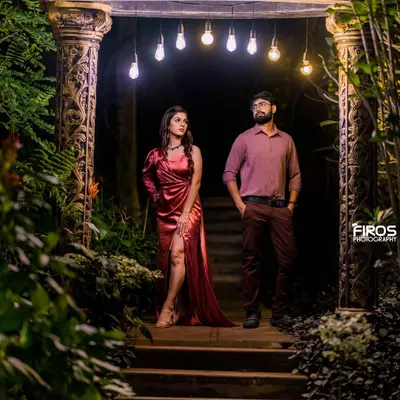 A moody and stylish night portrait. The couple stands under a row of Edison bulbs, creating a dramatic, low-light scene that feels both modern and intimate.