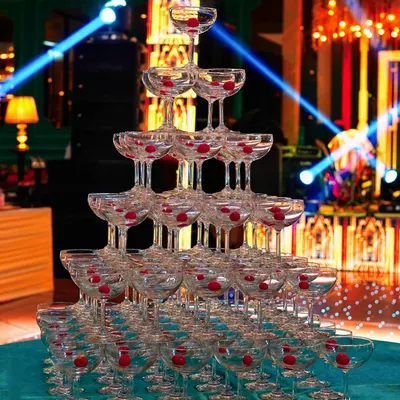 A magnificent champagne tower stands ready for the celebration. Lit by spotlights, the tower is built from dozens of glasses with cherries, waiting for the first pour.