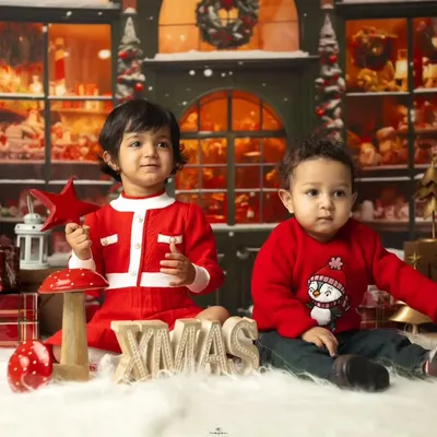 Two adorable children dressed in red for our Christmas-themed studio session. We use festive backdrops and props like wooden "XMAS" letters and reindeer to create a magical holiday scene.