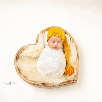 A perfect heart holding a perfect gift. This minimalist shot features a swaddled baby sleeping in a heart-shaped wooden bowl on a clean white background.